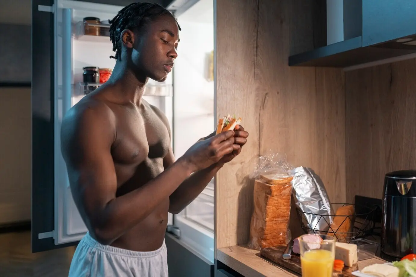 Hombre joven tomando un tentempié en medio de la noche en casa junto al refrigerador.