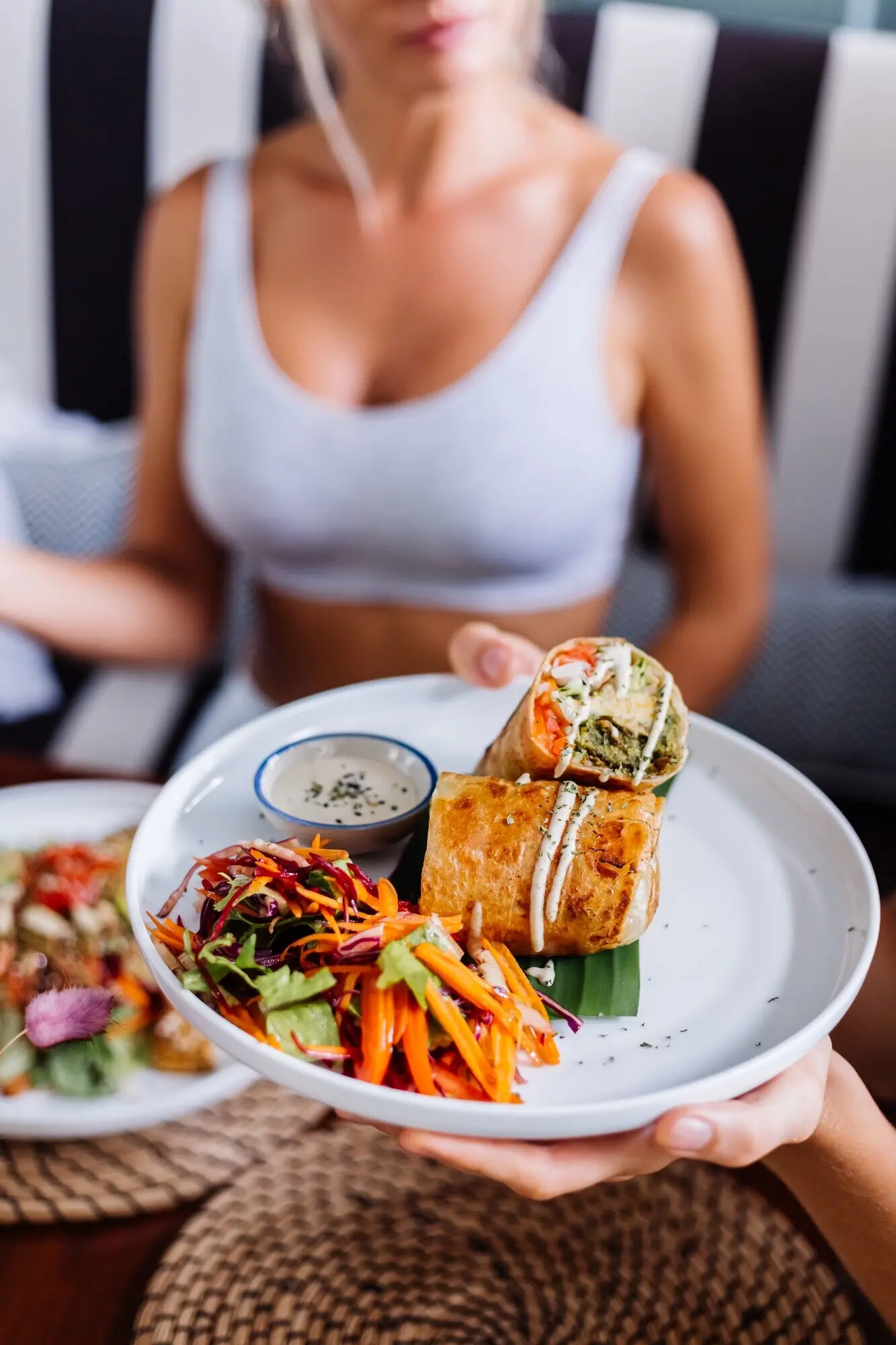 Mujer comiendo una ensalada colorida y saludable, vegana y vegetariana, en un café de verano con luz natural del día.